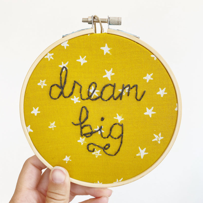 embroidery with hand-lettering that says dream big on mustard yellow fabric with white stars